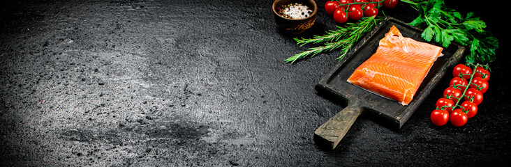 Salted salmon with greens and tomatoes on a cutting board.