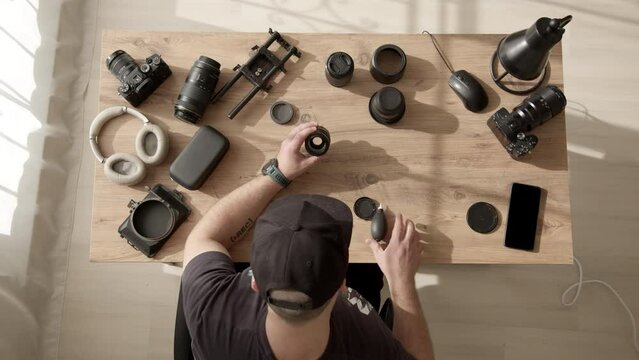 Top down view of desktop where videographer clean dust and dirt from equipment. man in cap work with lens from photo camera or video camera. photographer takes care of equipment. Lens repair service.