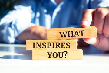 Close up on businessman holding a wooden block with "What Inspires You?" message