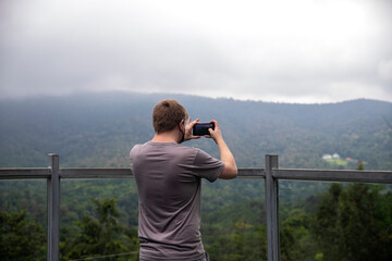 Fototapeta na wymiar A man taking photo of beautiful mountain landscape with mobile phone