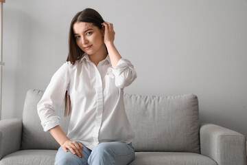 Young woman in white shirt sitting on sofa at home