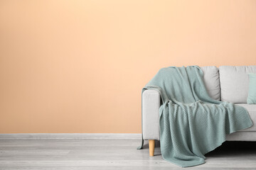 Cozy grey sofa with plaid near beige wall