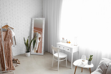 Interior of stylish makeup room with tables, mirror and clothes