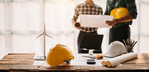 Engineer desk with object paper and tablet with blurry engineer teamwork hardworking to consults about their building project...