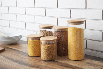 Jars with different cereals on wooden table near brick wall