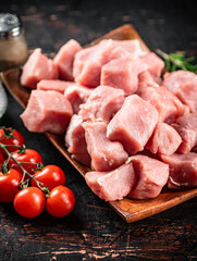 Pieces of raw pork on a wooden plate with spices and tomatoes. 