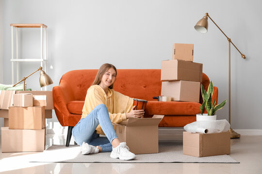 Young woman putting drum into cardboard box in living room on moving day