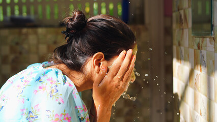 Beautiful woman is washing facial mask in bathroom after applying face mask. Girl spraying water on...