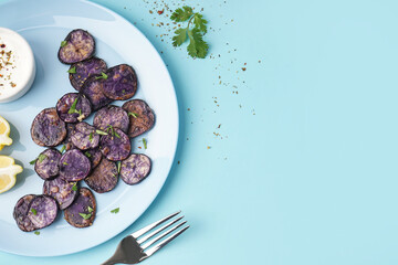 Plate with slices of fried purple potatoes on color background, closeup