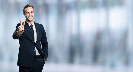 Excited businessman in black confident suit showing two fingers or victory sign gesture, over...