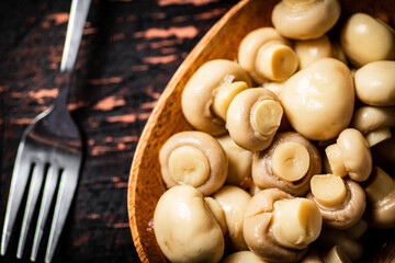 Pickled mushrooms in a wooden plate on the table. 