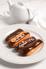 Plate with sweet chocolate eclairs on light background, closeup