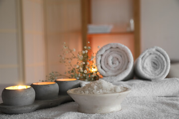 Fototapeta na wymiar Bowl of sea salt and burning candles on couch in spa salon, closeup