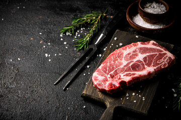 Raw pork steak on a cutting board with spices and rosemary. 