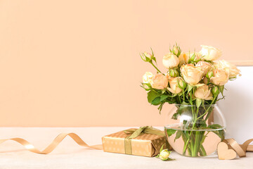 Vase with beautiful rose flowers and gift on table near color wall