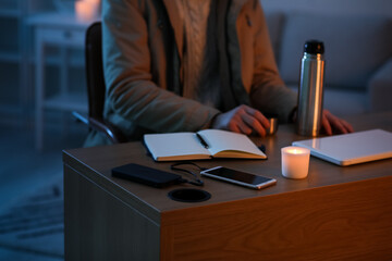 Power bank charging mobile phone on table of man with thermos in office during blackout, closeup