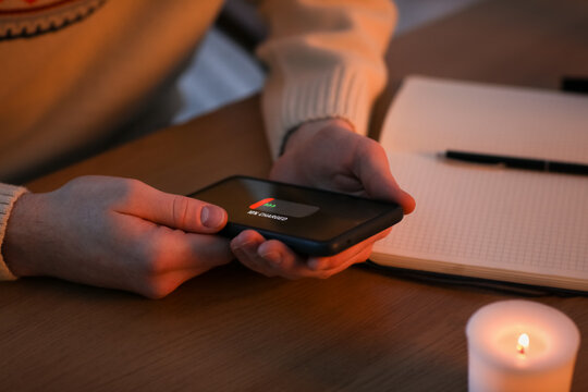 Young man with discharged mobile phone in office during blackout, closeup