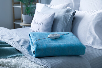 Folded electric heating pad with controller on bed in bedroom, closeup