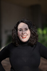 Fototapeta premium A woman with pale skin and black, wavy hair poses confidently outdoors.