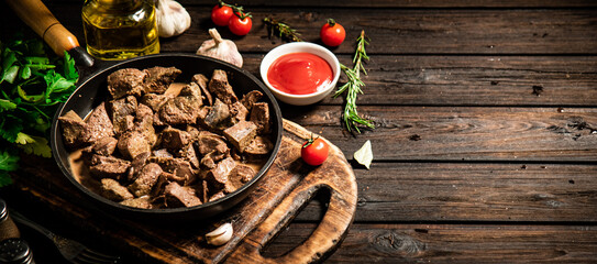 Fried liver in a frying pan on a cutting board with tomato sauce.