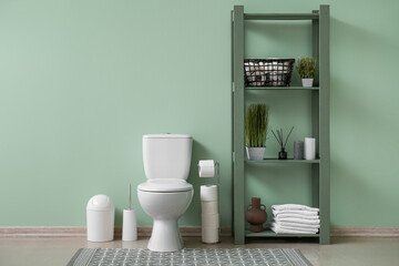 Interior of restroom with ceramic toilet bowl, rug and shelving unit near green wall