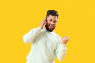 Happy young bearded man talking by mobile phone on yellow background