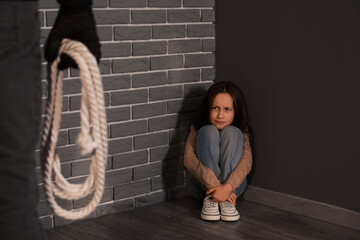 Terrorist with rope and scared little hostage sitting in corner