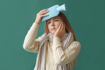 Ill girl warming her head with hot water bottle on green background
