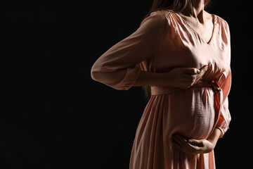 Young pregnant woman on dark background. Breast cancer awareness concept