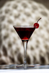 Black Manhattan cocktail with whiskey and red vermouth garnished with maraschino cocktail cherry in martini glass. Beige background, hard light and shaped shadows