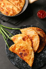Board with tasty chebureks on dark grunge background, closeup