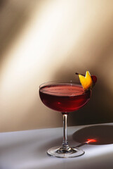 New Yorker cocktail with whiskey, grenadine, bitters, lemon juice and ice, garnished with lemon zest and cherries in glass. Beige background, hard light