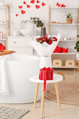 Vase with bouquet of flowers and gift on table in bathroom decorated for Valentine's Day