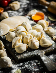 Raw dumplings on a cutting board with egg and flour. 