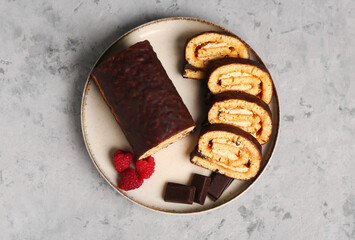 Plate with pieces of tasty sponge cake roll, chocolate and raspberry on grunge background