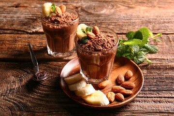 Glasses with delicious chocolate pudding, almond, banana and mint leaves on wooden background
