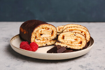 Plate with pieces of tasty sponge cake roll, chocolate and raspberry on grunge background