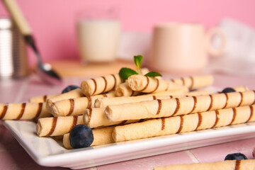 Plate with tasty wafer rolls, mint and blueberries on pink table, closeup