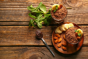 Glasses with delicious chocolate pudding, almond, banana and mint leaves on wooden background