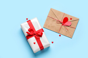 Gift box with beautiful bow, hearts and envelope on blue background. Valentine's Day celebration