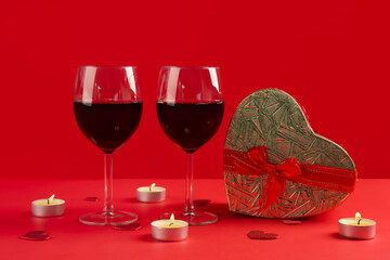 Glasses of wine, heart-shaped gift and burning candles on red background. Valentine's Day Celebration