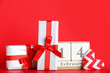 Gift boxes, decorative heart and cube calendar with date 14 FEBRUARY on red background. Valentine's Day celebration