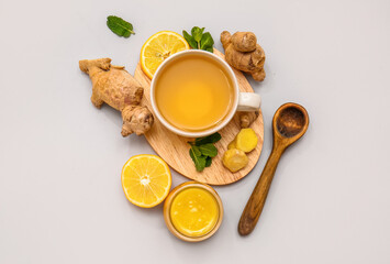Composition with cup of ginger tea, roots, honey, lemon and mint on grey background
