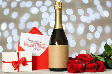 Bottle of wine, rose flowers, envelope and gift boxes on table against blurred lights. Valentine's Day celebration