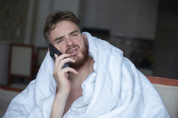 young unhappy angry annoyed man covering himself in blanket with sad frustrated look at home in...