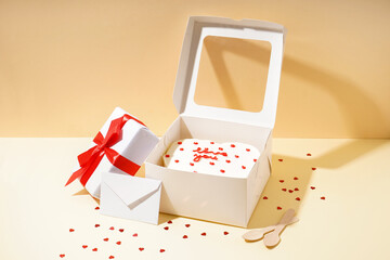 Opened box with tasty bento cake, gift and envelope on beige table. Valentine's Day celebration