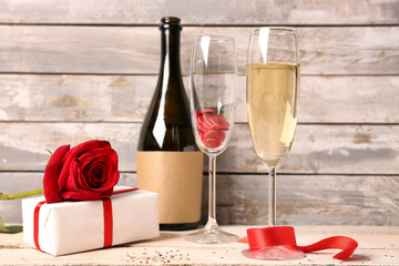 Glasses of champagne, bottle, gift box and rose flower on white wooden table. Valentine's Day celebration