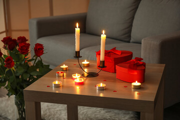 Burning candles and gifts for Valentine's Day on table in dark living room