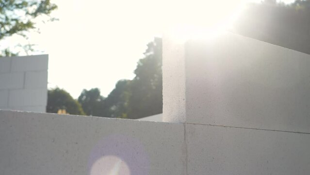 Sun shines over grey brick wall and working hand removes one block from the top. Human hand building a wall structure on a garden terrace. Use and work with hardscape materials at building project.