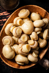 Pickled mushrooms in a wooden plate on the table. 